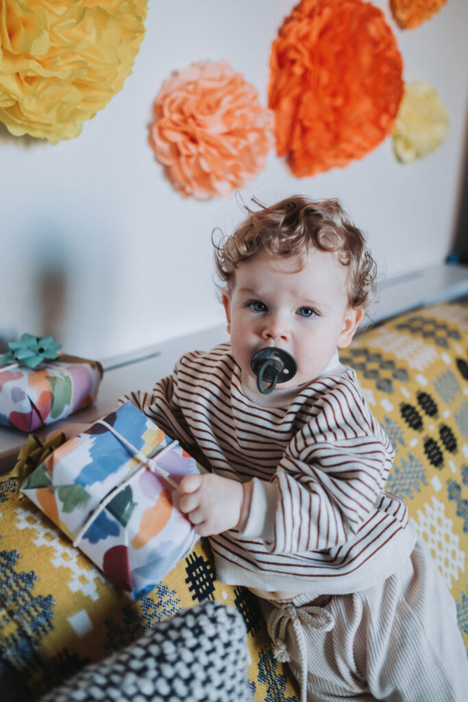 Curly hair little boy with a pacifier holds a wrapped birthday present 