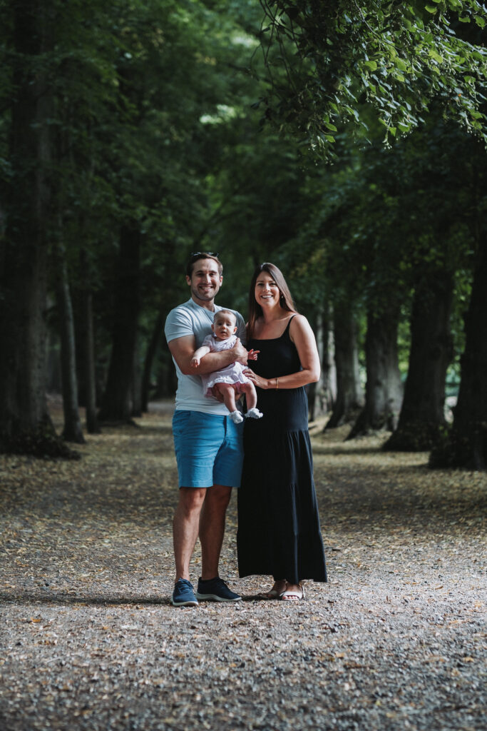 Family of three stand in a wooden path in a part of Hampstead Heath London