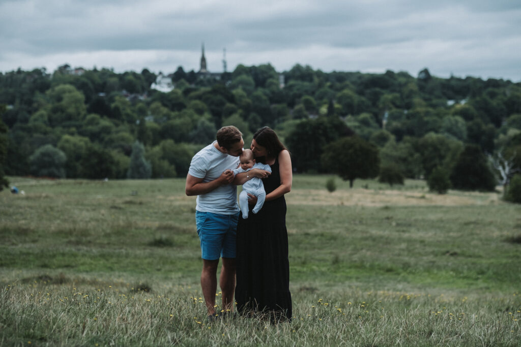 Mother and father kiss their baby daughter at Hampstead Heath in London