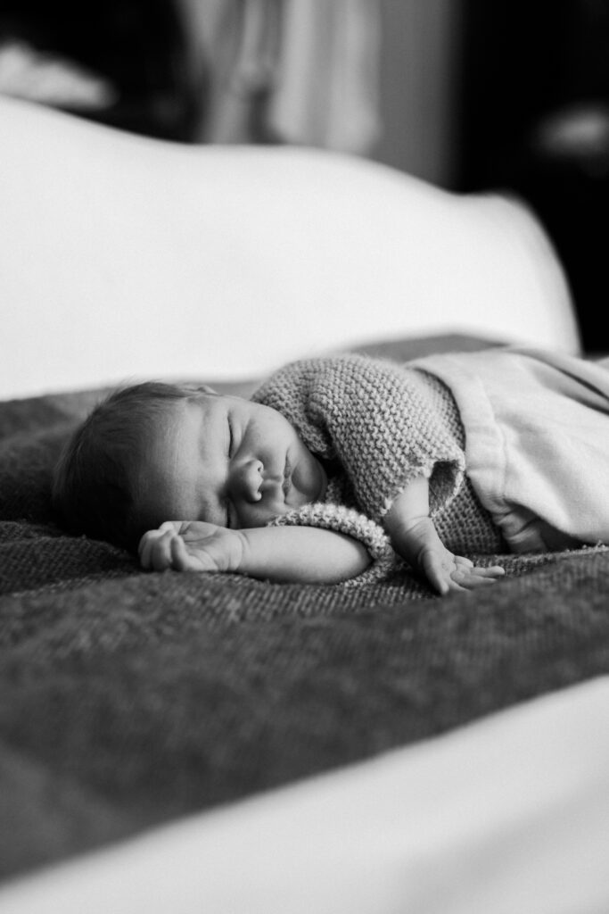 A newborn baby in London wearing a knit jumper sleeps in bed