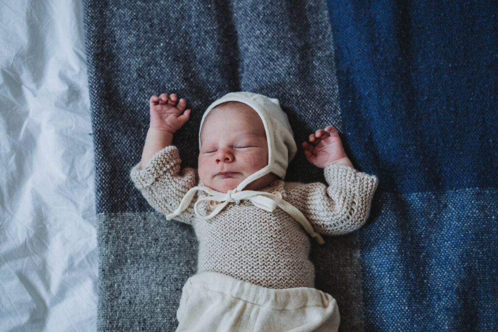 Sweet sleeping newborn baby wearing a bonnet rests on a wool blanket in bed in London