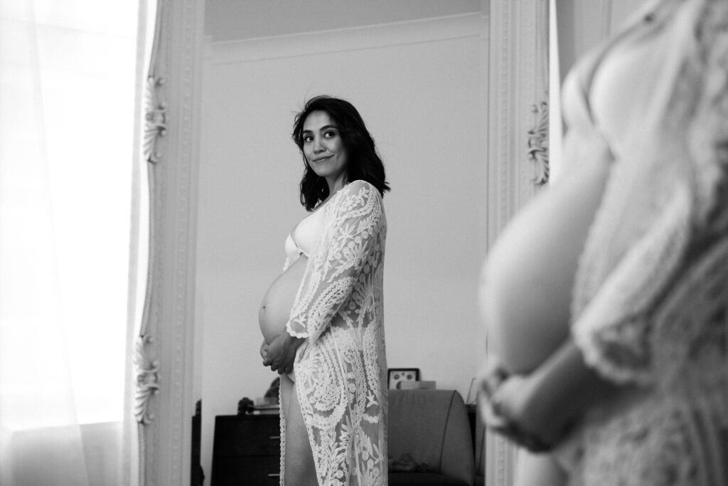 Smiling pregnant woman looks at herself in the mirror during photoshoot at her home in London